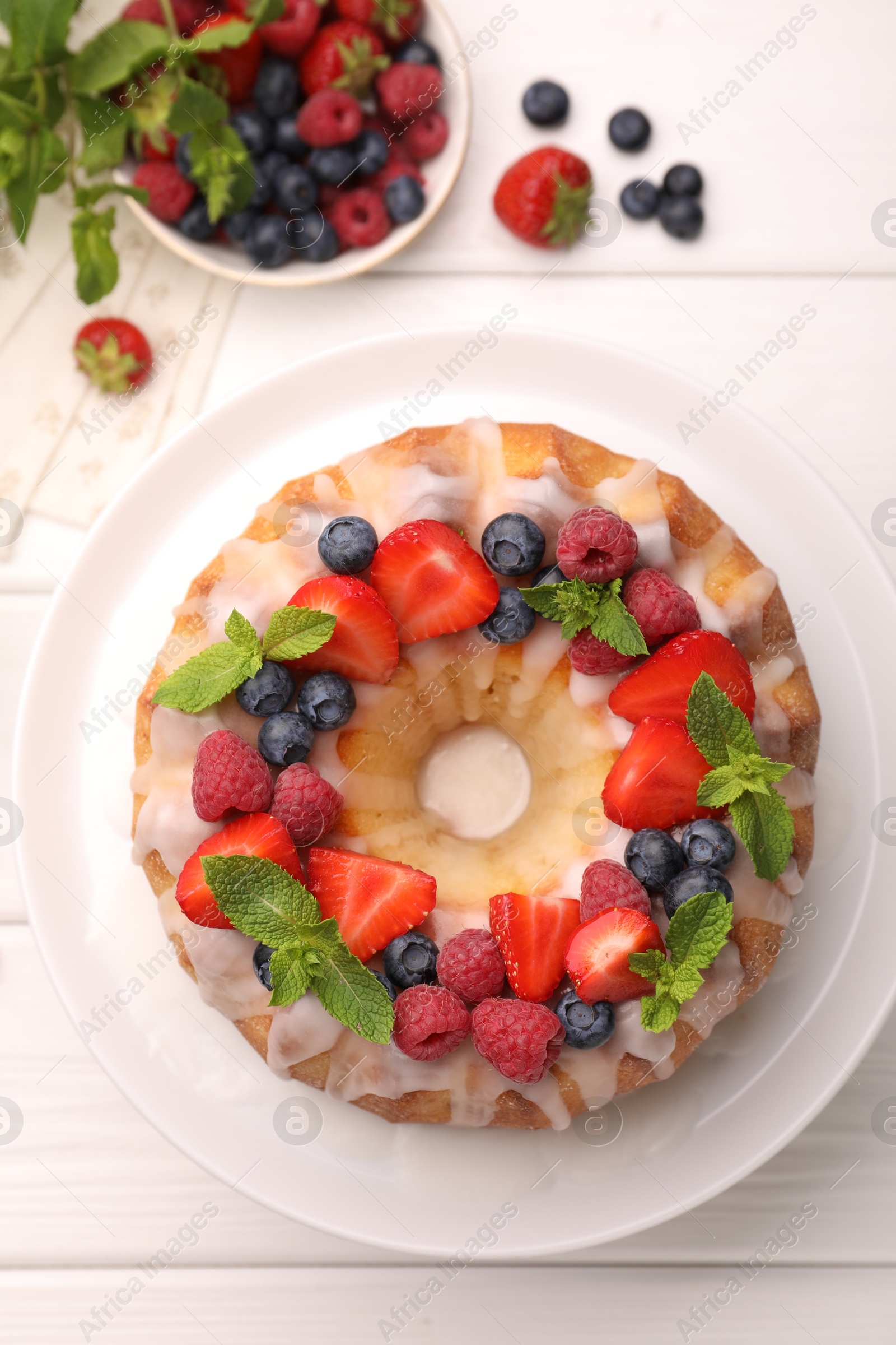 Delicious bundt cake with berries, glaze and mint on white wooden table, flat lay Photo of Delicious bundt cake with berries, glaze and mint on white wooden table, flat lay