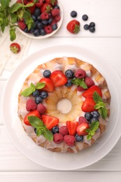 Photo of Delicious bundt cake with berries, glaze and mint on white wooden table, flat lay