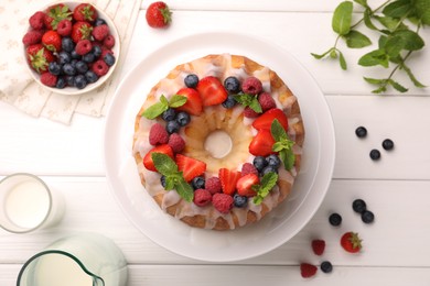Photo of Delicious bundt cake with berries, glaze and mint on white wooden table, flat lay