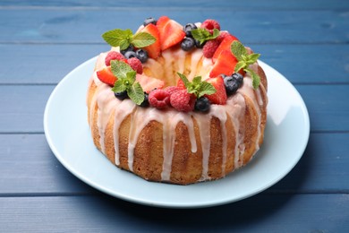 Photo of Delicious bundt cake with berries, glaze and mint on blue wooden table, closeup