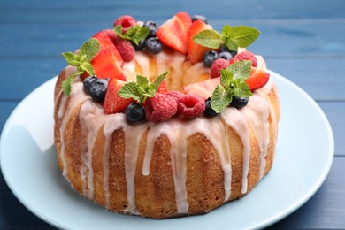 Photo of Delicious bundt cake with berries, glaze and mint on blue wooden table, closeup