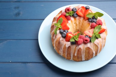 Photo of Delicious bundt cake with berries, glaze and mint on blue wooden table, closeup