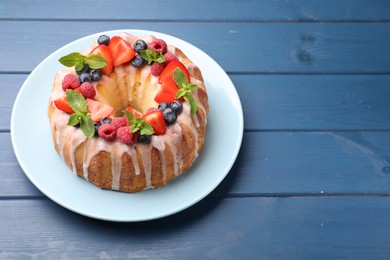 Photo of Delicious bundt cake with berries, glaze and mint on blue wooden table