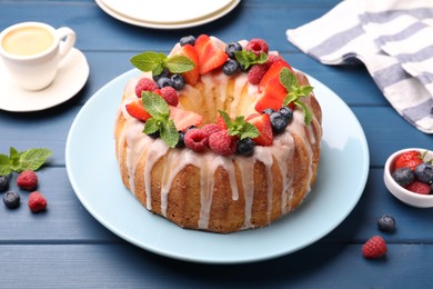 Photo of Delicious bundt cake with berries, glaze and mint on blue wooden table, closeup