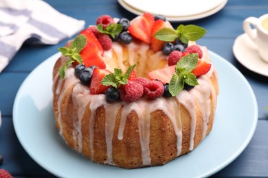 Photo of Delicious bundt cake with berries, glaze and mint on blue wooden table, closeup