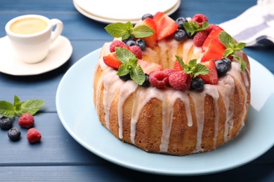 Photo of Delicious bundt cake with berries, glaze and mint on blue wooden table, closeup