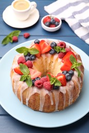 Photo of Delicious bundt cake with berries, glaze and mint on blue wooden table, closeup