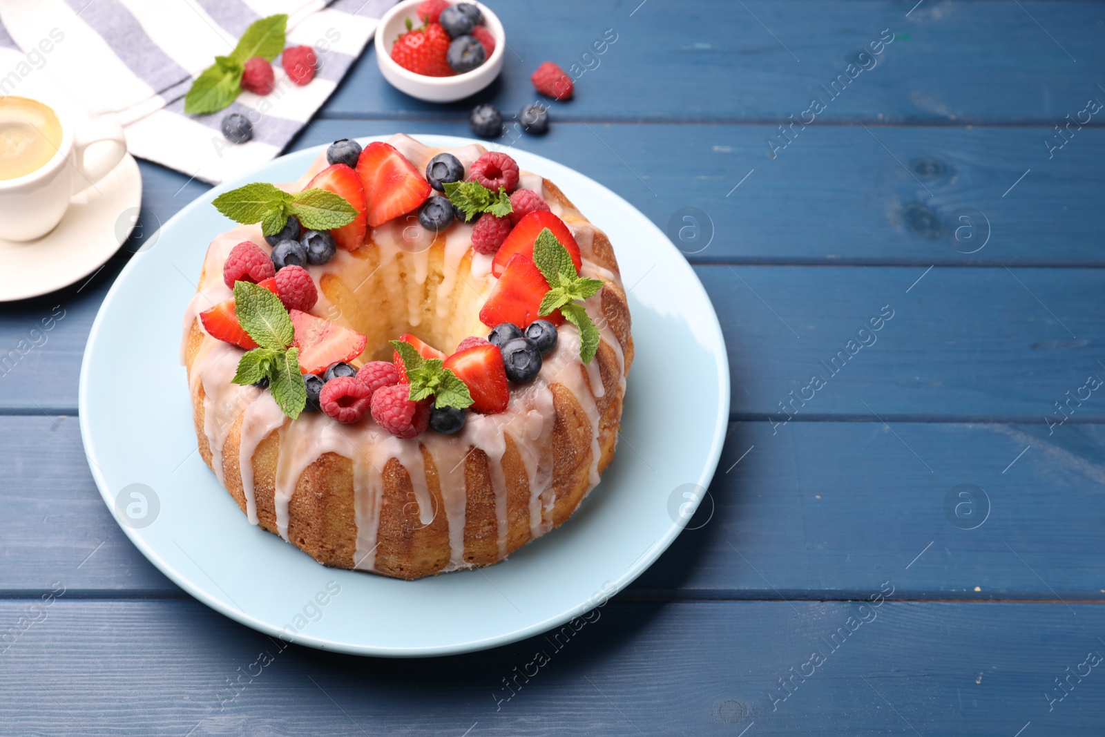 Photo of Delicious bundt cake with berries, glaze and mint on blue wooden table, closeup