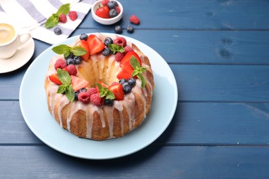Photo of Delicious bundt cake with berries, glaze and mint on blue wooden table, closeup