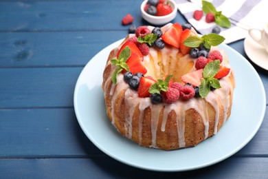 Photo of Delicious bundt cake with berries, glaze and mint on blue wooden table, closeup