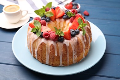 Photo of Delicious bundt cake with berries, glaze and mint on blue wooden table, closeup