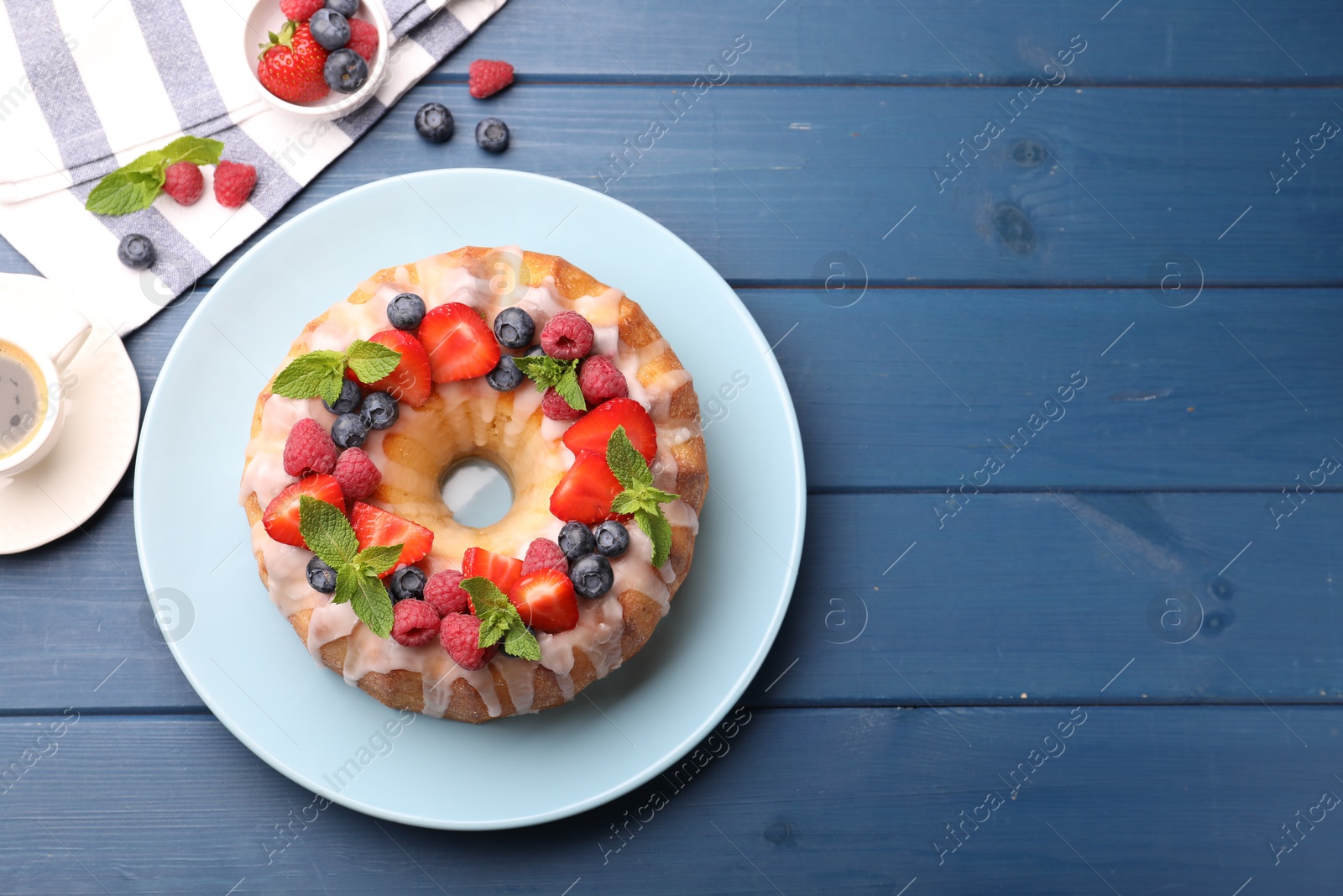 Delicious bundt cake with berries, glaze and mint on blue wooden table, flat lay. Space for text Photo of Delicious bundt cake with berries, glaze and mint on blue wooden table, flat lay. Space for text