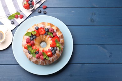 Photo of Delicious bundt cake with berries, glaze and mint on blue wooden table, flat lay. Space for text