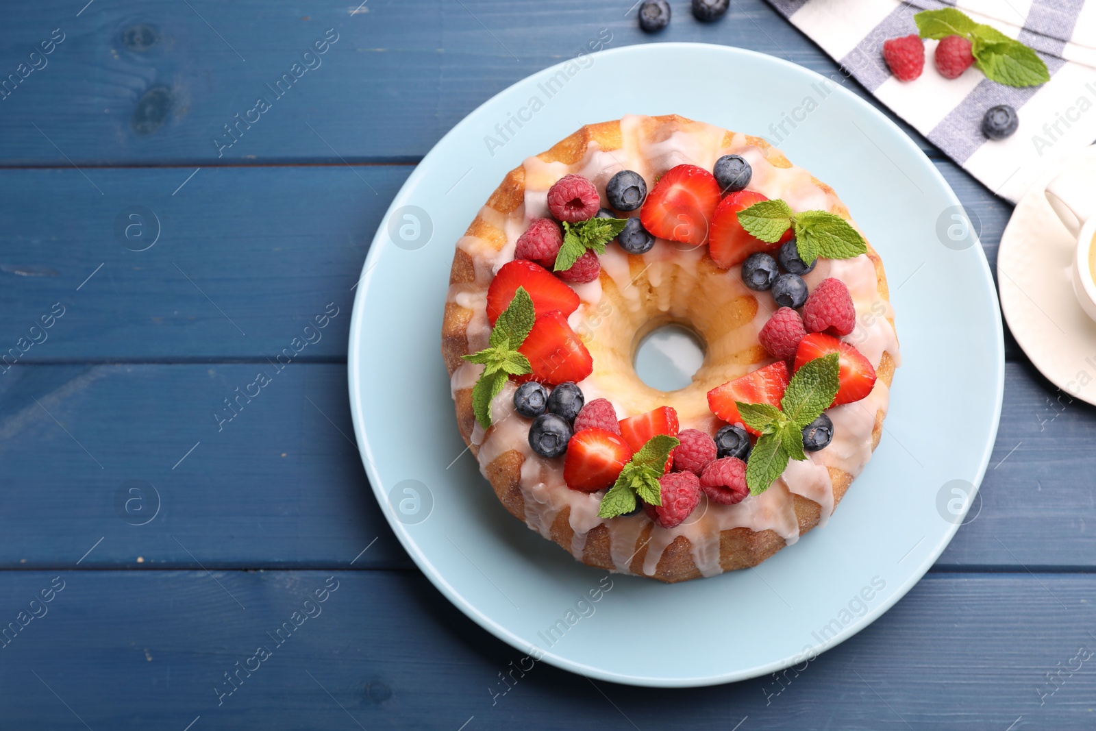 Delicious bundt cake with berries, glaze and mint on blue wooden table, flat lay. Space for text Photo of Delicious bundt cake with berries, glaze and mint on blue wooden table, flat lay. Space for text