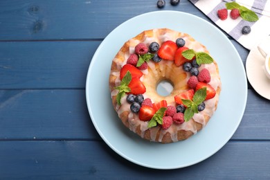 Photo of Delicious bundt cake with berries, glaze and mint on blue wooden table, flat lay. Space for text