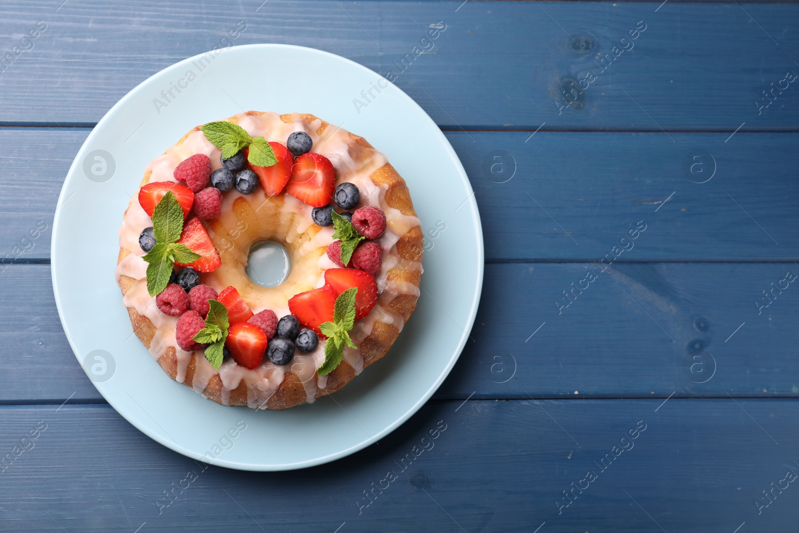 Delicious bundt cake with berries, glaze and mint on blue wooden table, top view. Space for text Photo of Delicious bundt cake with berries, glaze and mint on blue wooden table, top view. Space for text