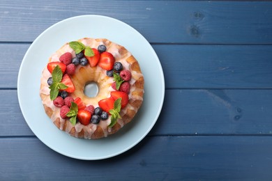 Photo of Delicious bundt cake with berries, glaze and mint on blue wooden table, top view. Space for text