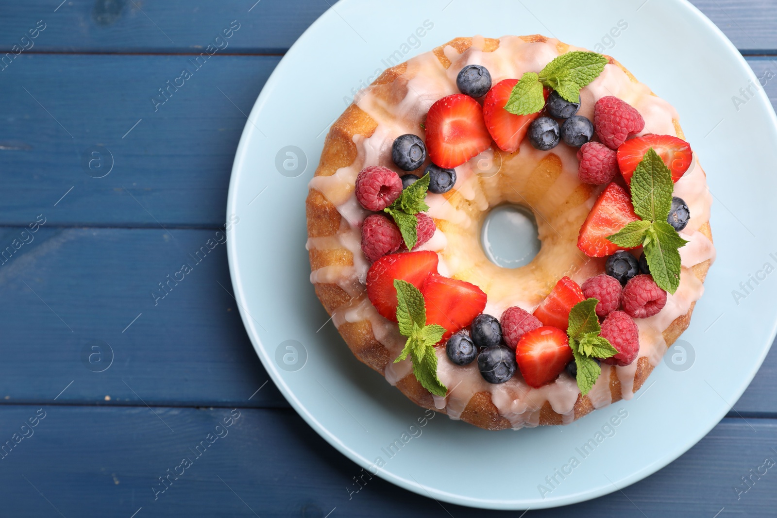 Delicious bundt cake with berries, glaze and mint on blue wooden table, top view. Space for text Photo of Delicious bundt cake with berries, glaze and mint on blue wooden table, top view. Space for text