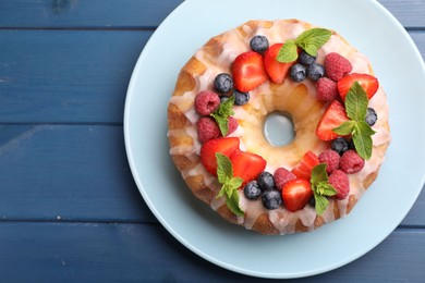 Photo of Delicious bundt cake with berries, glaze and mint on blue wooden table, top view. Space for text