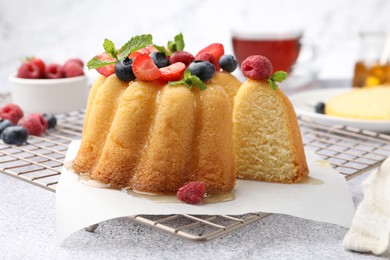 Photo of Tasty Bundt cake with berries, honey and mint on light grey table, closeup