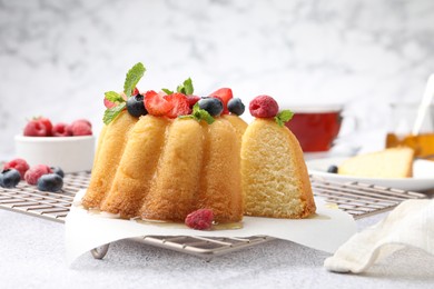 Photo of Tasty Bundt cake with berries, honey and mint on light grey table, closeup