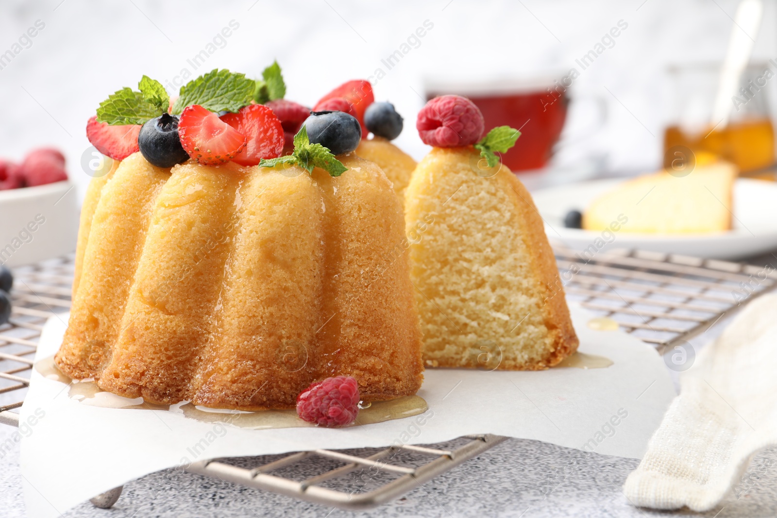 Photo of Tasty Bundt cake with berries, honey and mint on light grey table, closeup