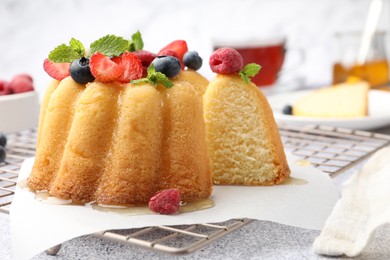 Photo of Tasty Bundt cake with berries, honey and mint on light grey table, closeup