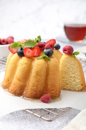 Photo of Tasty Bundt cake with berries, honey and mint on light grey table, closeup