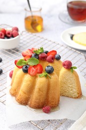 Photo of Tasty Bundt cake with berries, honey and mint on table, closeup