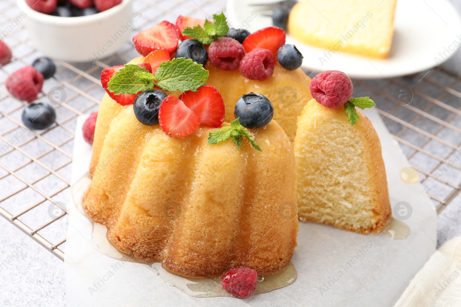 Tasty Bundt cake with berries, honey and mint on light grey table, closeup Photo of Tasty Bundt cake with berries, honey and mint on light grey table, closeup