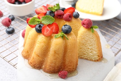 Photo of Tasty Bundt cake with berries, honey and mint on light grey table, closeup