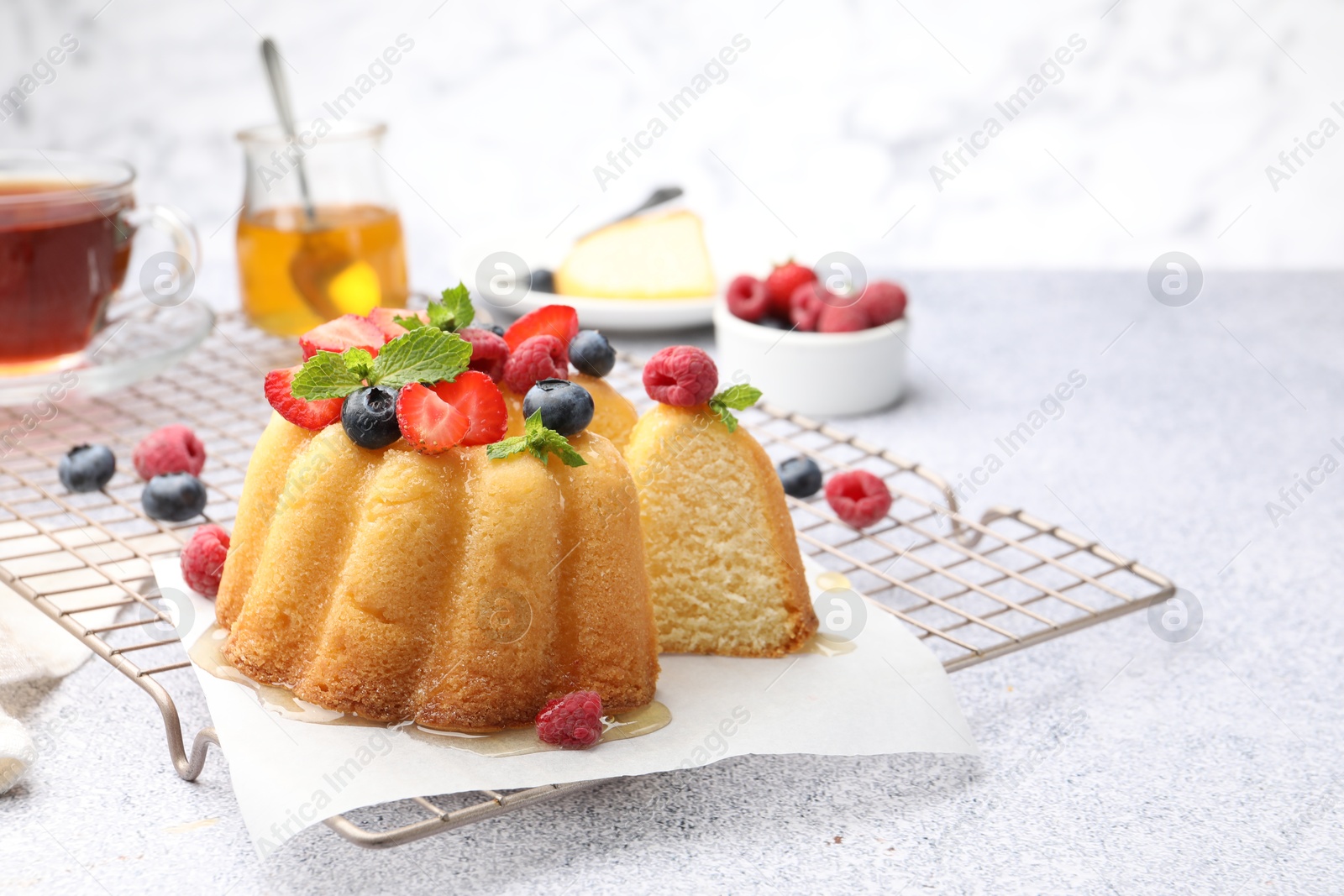 Tasty Bundt cake with berries, honey and mint on light grey table, closeup Photo of Tasty Bundt cake with berries, honey and mint on light grey table, closeup