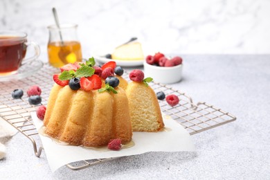 Photo of Tasty Bundt cake with berries, honey and mint on light grey table, closeup