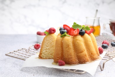 Photo of Tasty Bundt cake with berries, honey and mint on light grey table, closeup