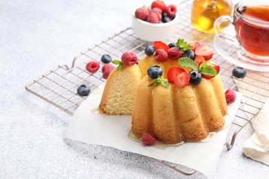 Photo of Tasty Bundt cake with berries, honey, mint and tea on light grey table, closeup