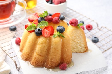Photo of Tasty Bundt cake with berries, honey, mint and tea on light grey table, closeup