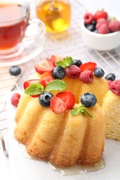 Photo of Tasty Bundt cake with berries, honey, mint and tea on table, closeup