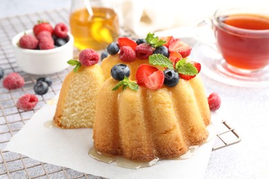 Photo of Tasty Bundt cake with berries, honey, mint and tea on light grey table, closeup