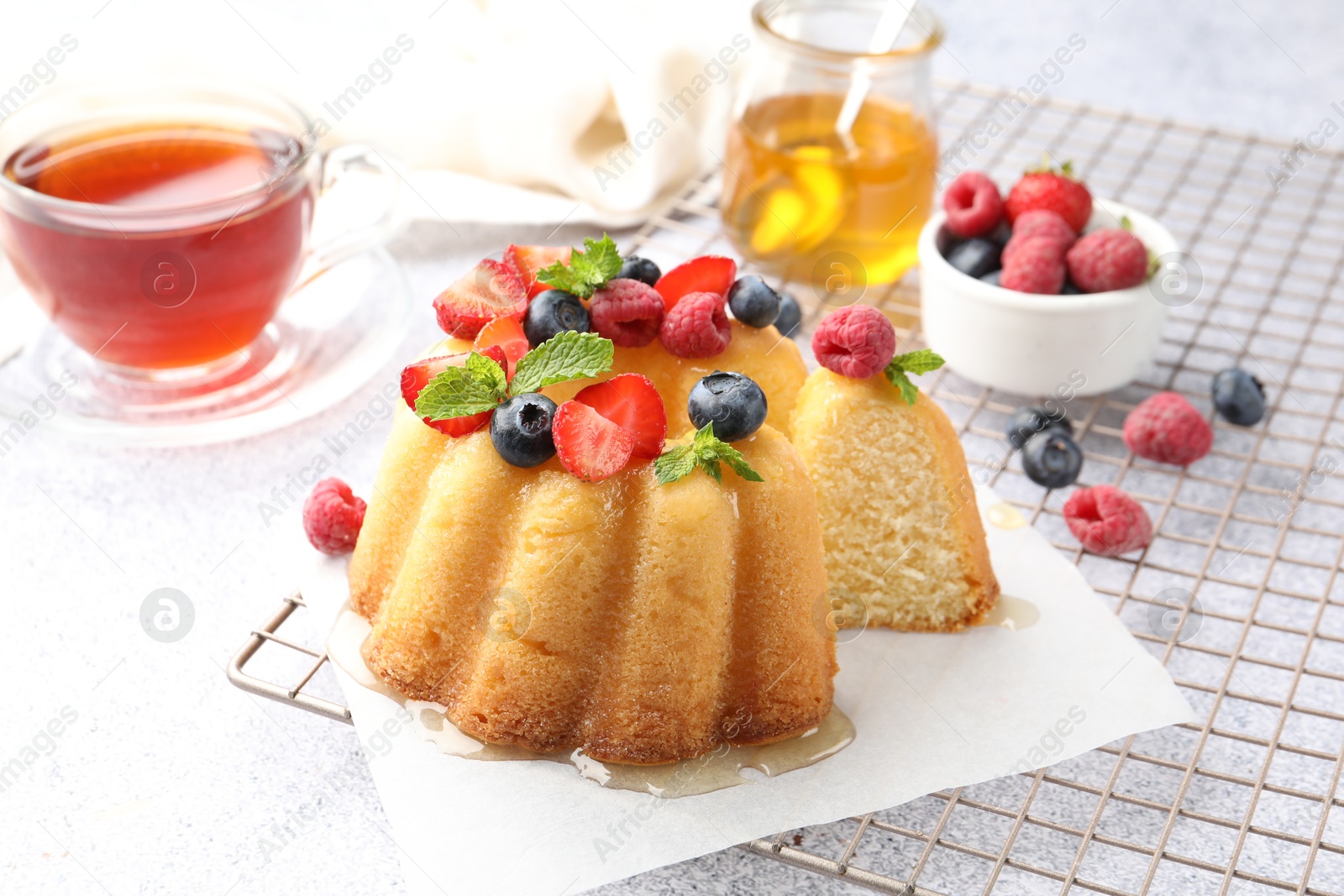 Photo of Tasty Bundt cake with berries, honey, mint and tea on light grey table, closeup