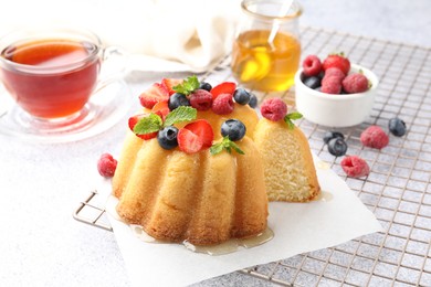 Photo of Tasty Bundt cake with berries, honey, mint and tea on light grey table, closeup