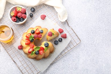 Photo of Tasty Bundt cake with berries, honey and mint on light grey table, flat lay. Space for text