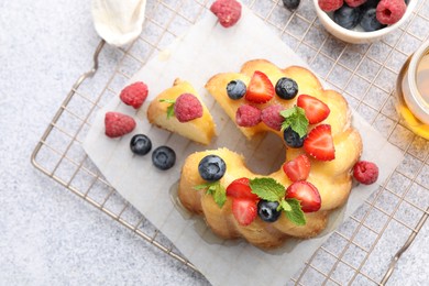 Photo of Tasty Bundt cake with berries, honey and mint on light grey table, flat lay