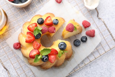 Photo of Tasty Bundt cake with berries, honey and mint on light grey table, flat lay