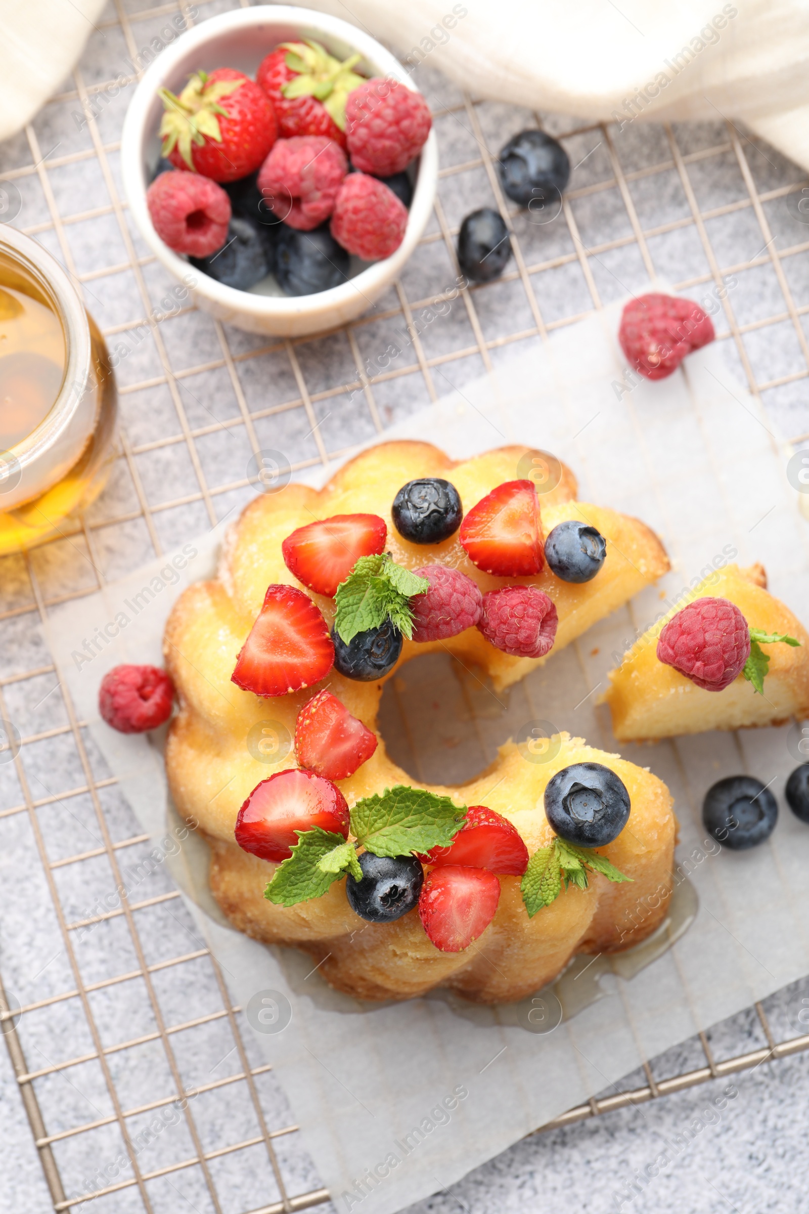 Tasty Bundt cake with berries, honey and mint on light grey table, flat lay Photo of Tasty Bundt cake with berries, honey and mint on light grey table, flat lay
