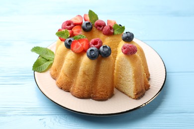 Photo of Tasty Bundt cake with berries and mint on light blue wooden table, closeup
