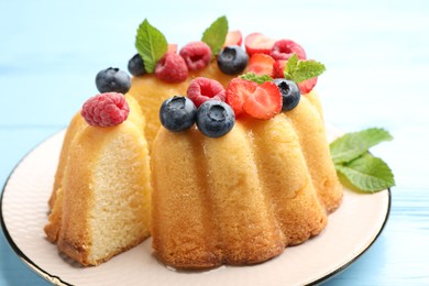 Photo of Tasty Bundt cake with berries and mint on light blue wooden table, closeup