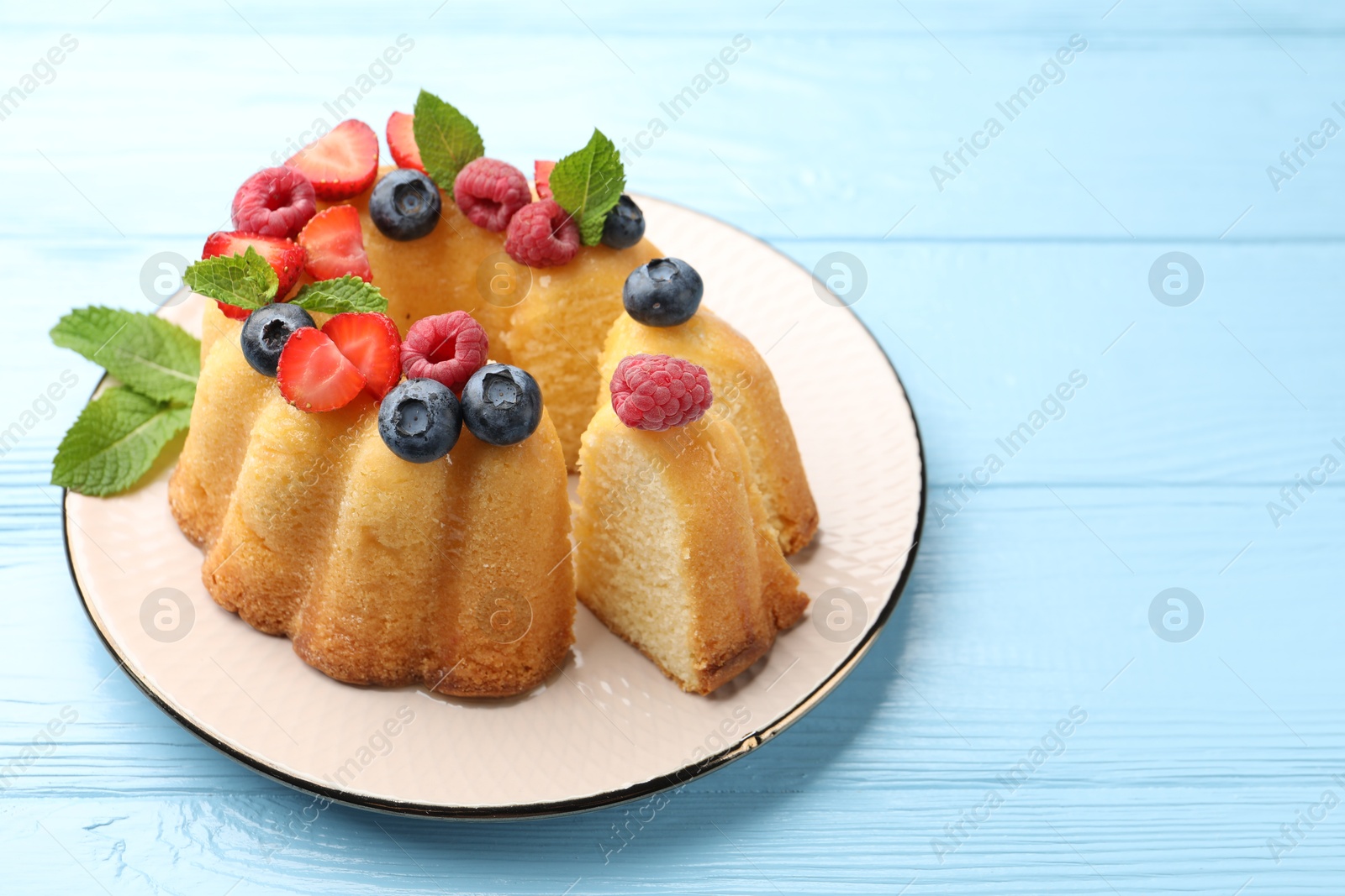 Photo of Tasty Bundt cake with berries and mint on light blue wooden table, closeup. Space for text