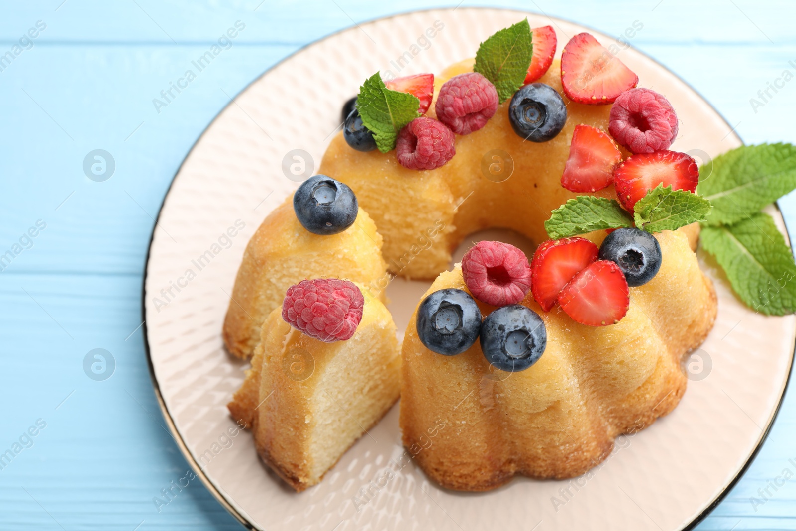 Tasty Bundt cake with berries and mint on light blue wooden table, above view Photo of Tasty Bundt cake with berries and mint on light blue wooden table, above view