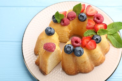 Photo of Tasty Bundt cake with berries and mint on light blue wooden table, above view
