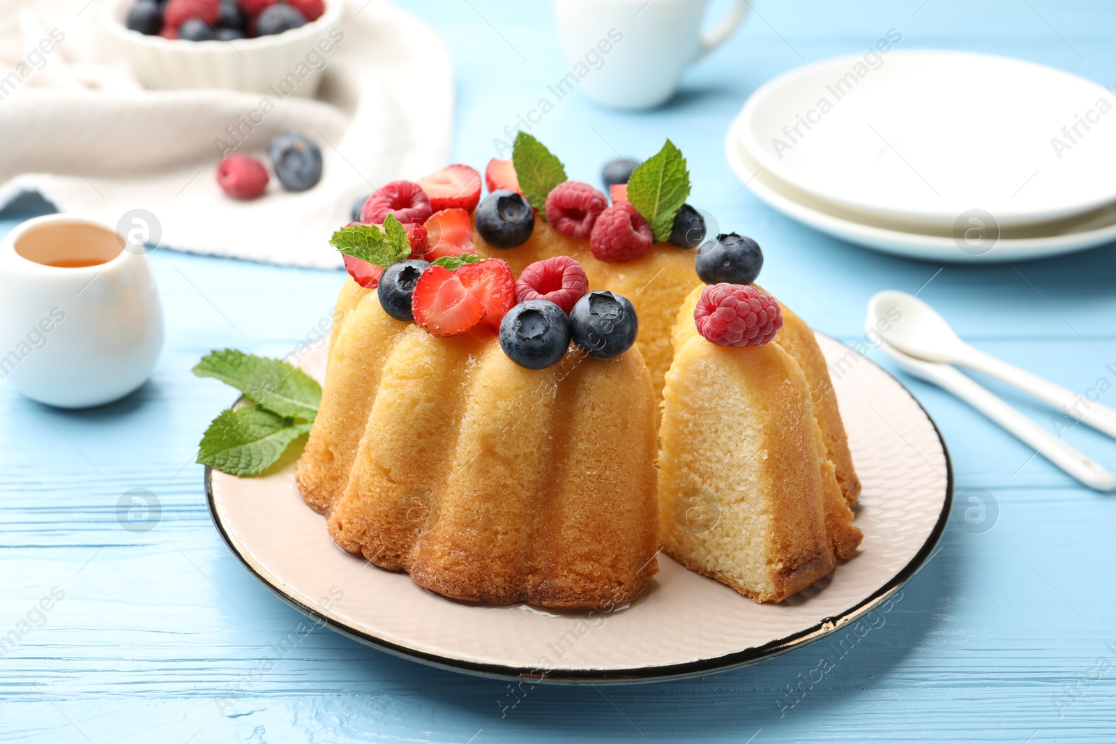 Photo of Tasty Bundt cake with berries, honey and mint on light blue wooden table, closeup